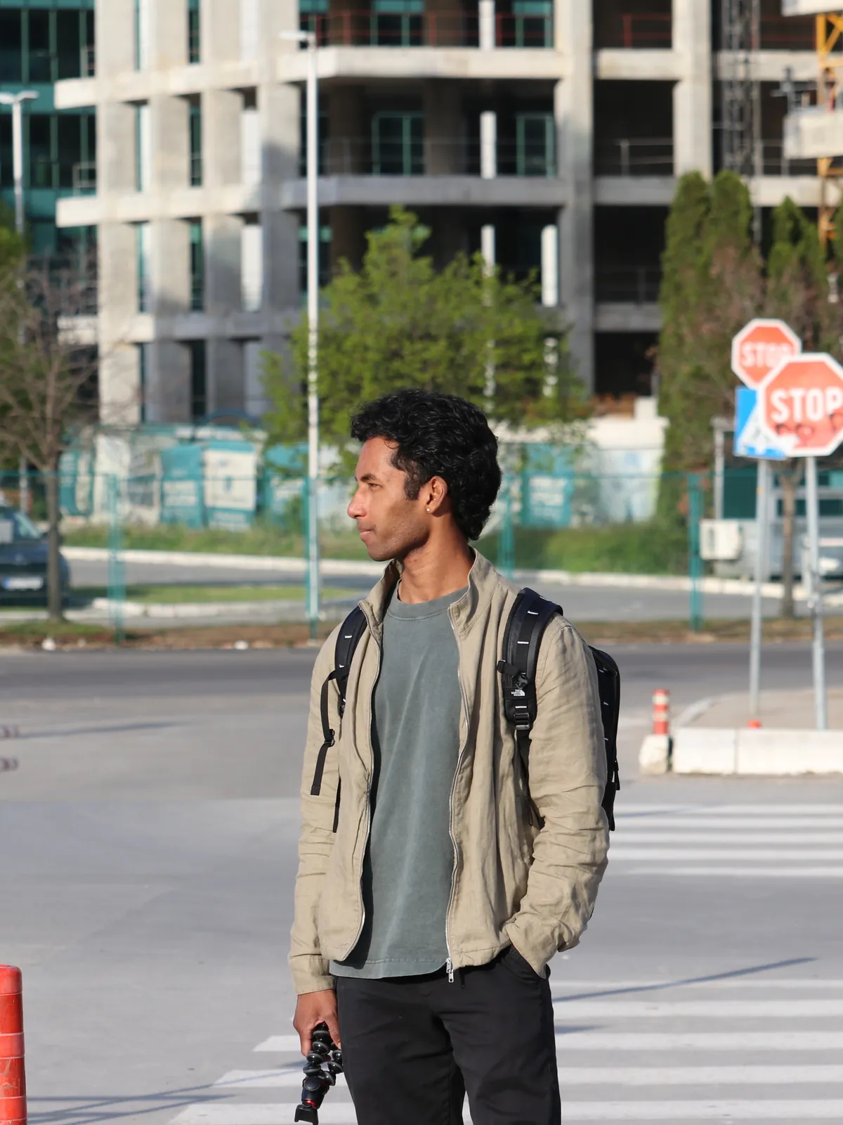 Sai at a city crosswalk in a beige jacket with a camera