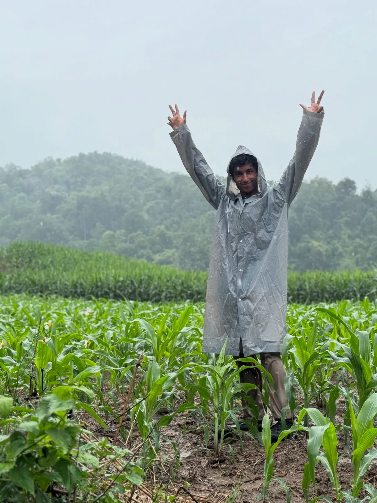 Sai with arms up in a rain poncho in a field